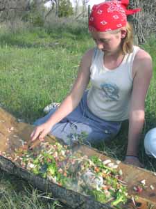 Student stiring food around hot rock on wood bark.